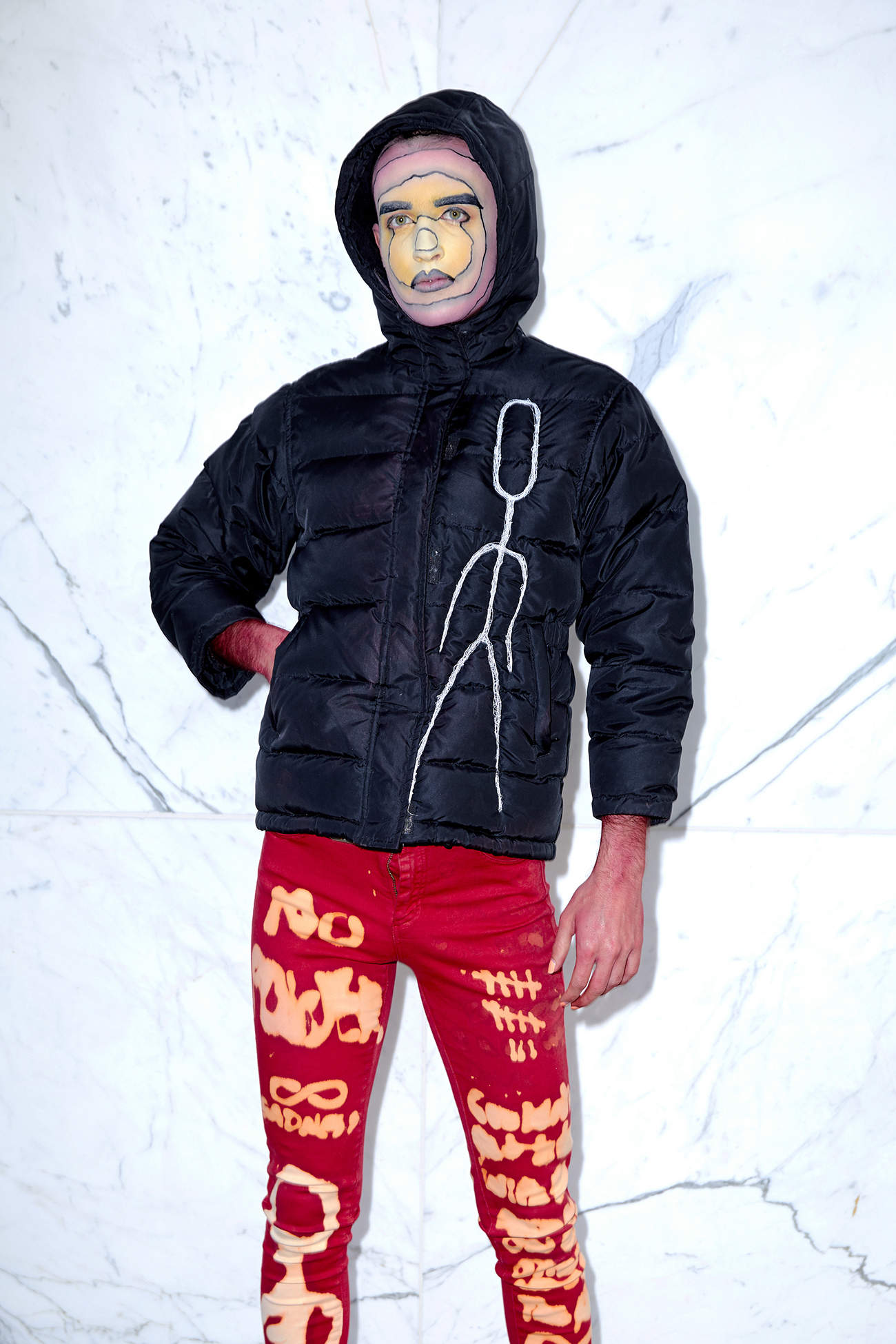 Jesse with red and yellow facepaint wearing a black puffer jacket against a marble background